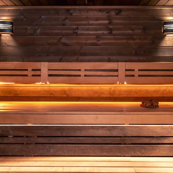 Wide shot of an empty sauna with wooden benches and soft lighting. Clean interior, huge vibe, wellness and detox without rush.
